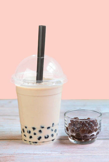 A plastic cup with bubble tea and a large straw next to a small bowl of boba pearls